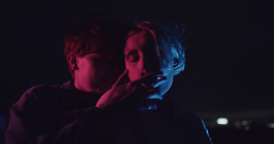 A couple dance closely while smoking cigarettes on their building rooftop