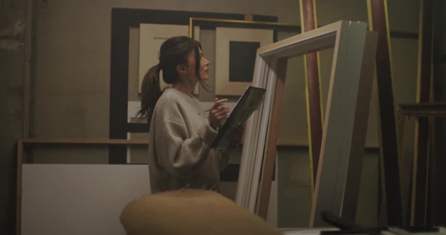 A young woman walks over to inspect a stack of large frames that are stacked up
