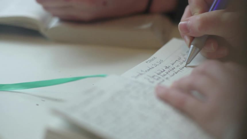 A person writes with a pen in a book