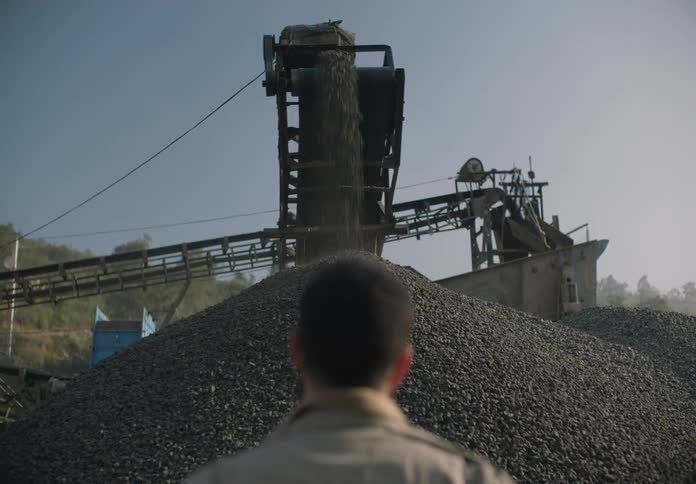 A man stands at a mining site and watches rocks move through a machine