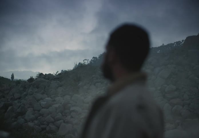 A man stands at the bottom of a pile of rocks and looks around