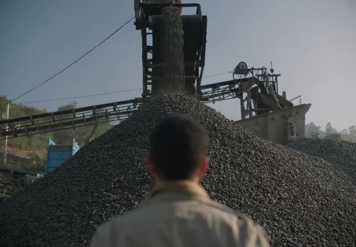 A man watching heavy outdoor machinery dump rocks into a large pile