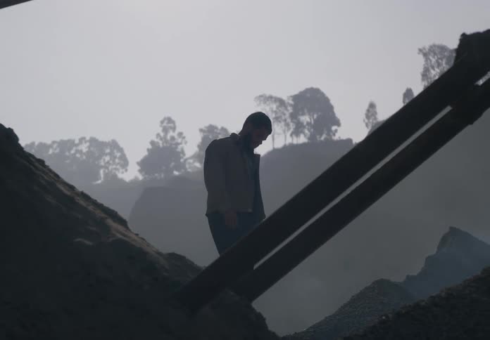 A man walks up a hill of dirt on a construction site and looks around
