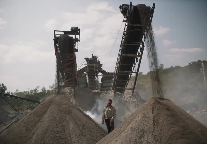 A man watches as gravel is poured onto mounds at a construction site
