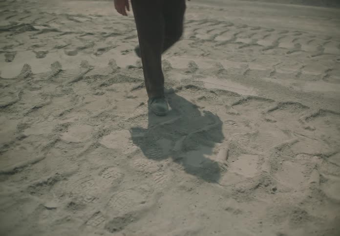 Tire tracks are in the dirt as smoke blows by and someone walks across the ground