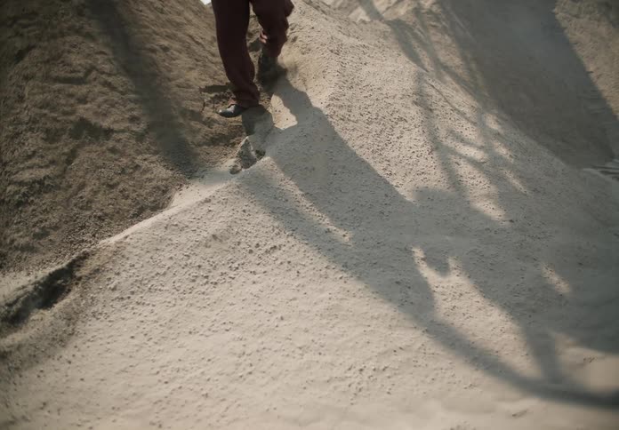 Man walks down dirt slope as shadow shows flow of material being poured