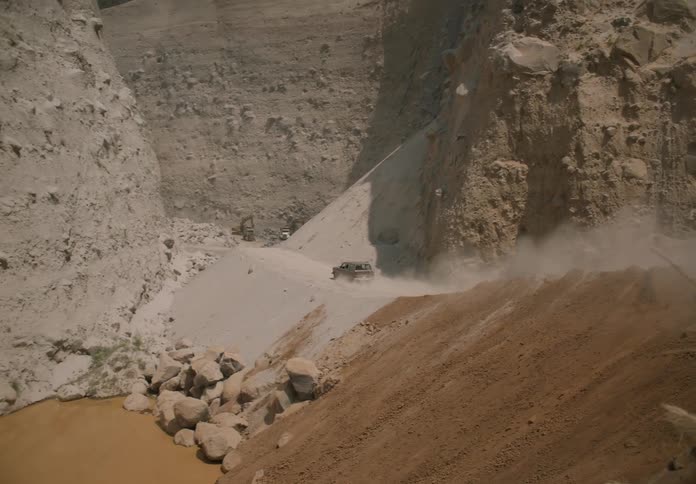 A truck travels on a desert mountain road as it leaves a trail of smoke and dust as it moves