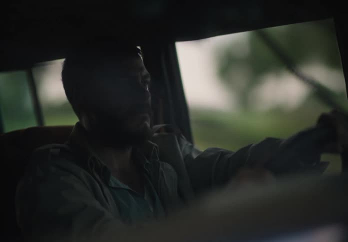 A man is holding the steering wheel with both hands as he drives through the country and occasionally looks out his side window