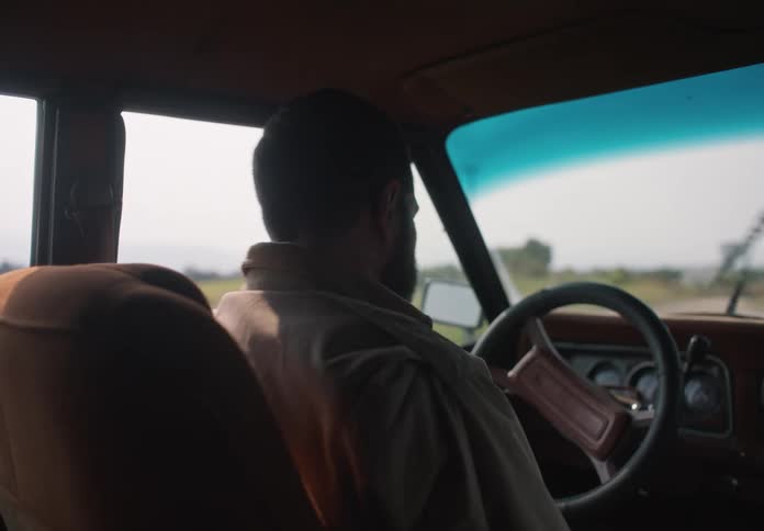 A man is driving an automobile and he stops and gets out leaving the door open as he walks away