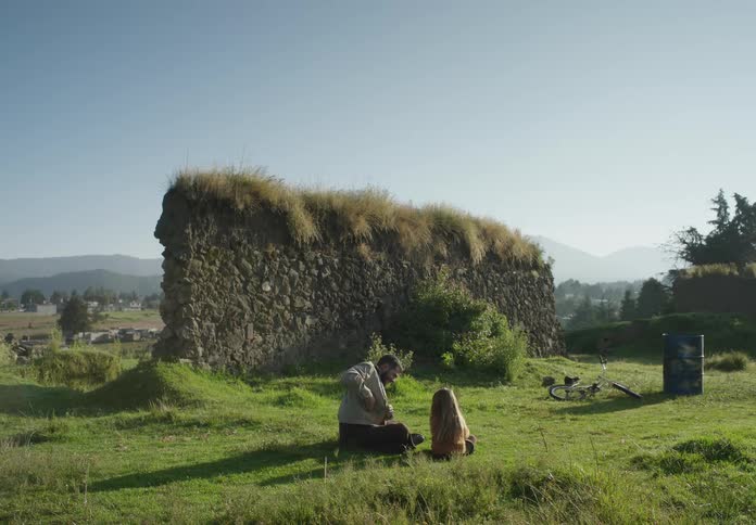 Father plays with daughter as they sit on ground behind stone wall overlooking town in valley