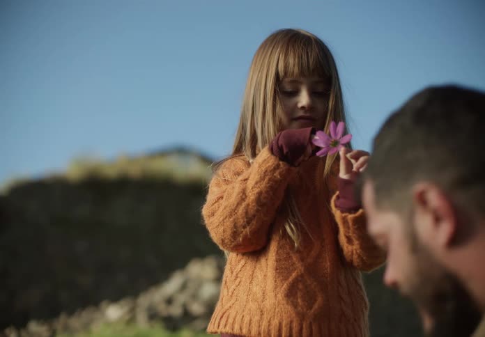 A young girl holds a flower and shows it to her father