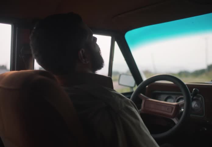 A man drives his car through a rural area and then pulls over takes a deep breath and gets out of the car