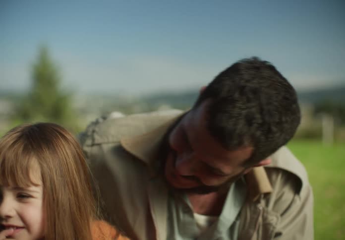 A father hugs his daughter as they sit in a field and talk