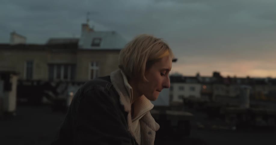 Two females sit atop the roof of a building while sharing beers and food