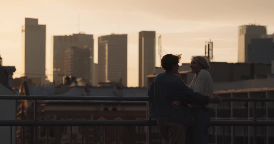 Young happy couple look at the city skyline at evening from the rooftop of a building