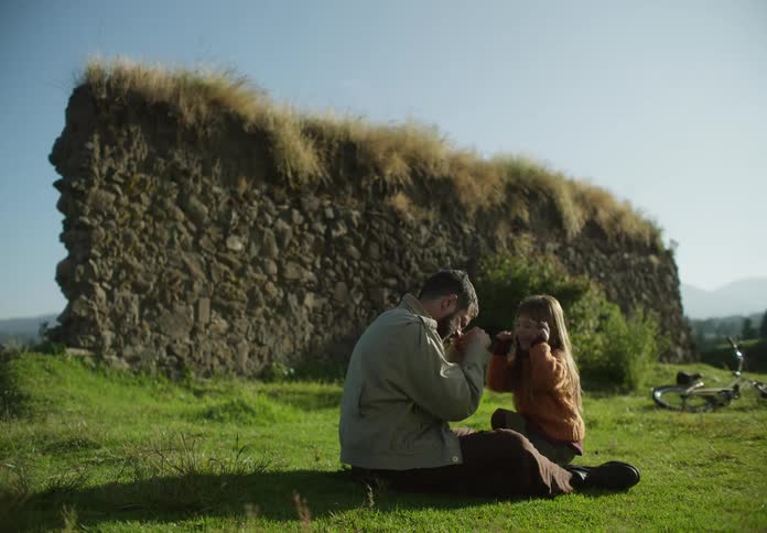 A man and his daughter make funny faces at each other while sitting outside