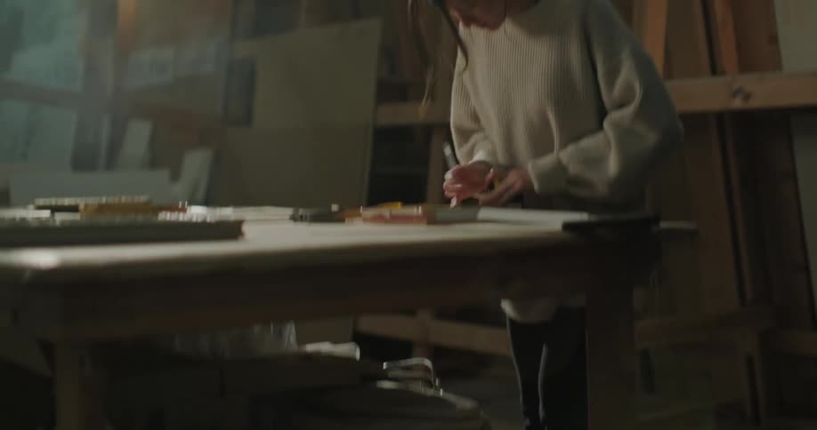 A woman making measurements while standing at a workshop table
