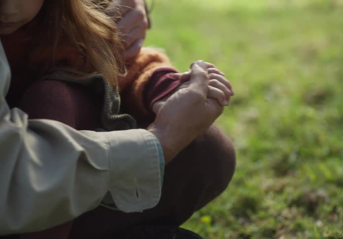 Father clutches daughter to his chest and holds her hand as they sit on ground