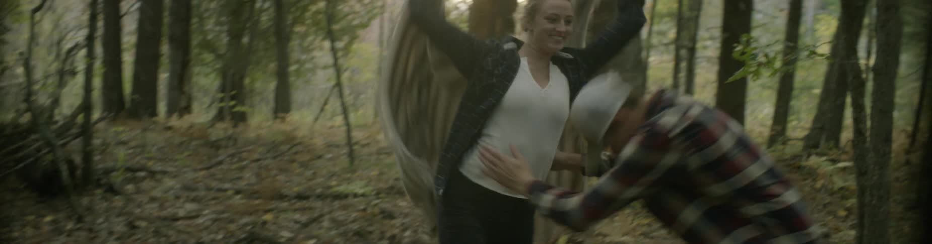 A man and woman chase and play in a forest