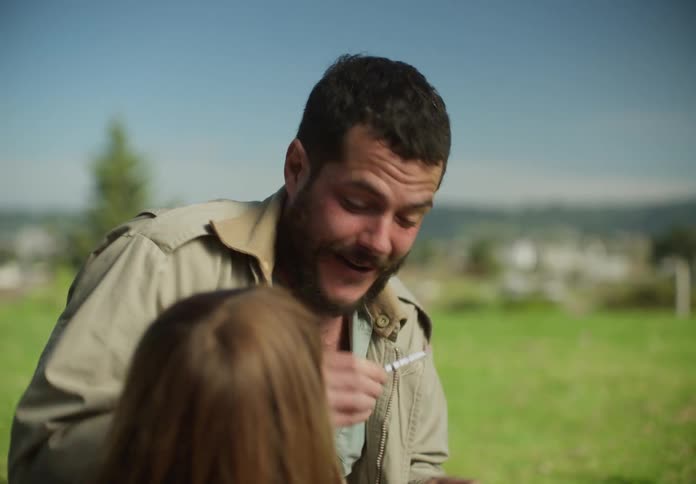 A man is outside with his young daughter and he lets her hold a firecracker before he lights it and throws it
