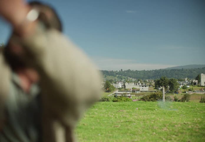 A man is outside in a field talking to his young daughter as he lights a firecracker and throws it then he gives her a hug