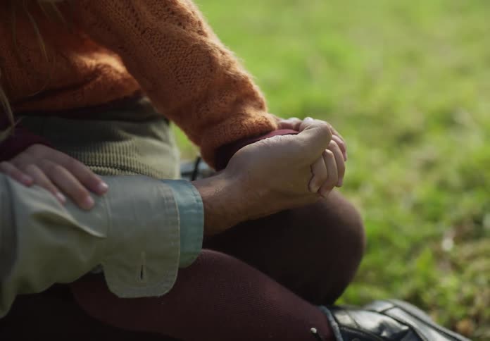 A young girl jumps in to the lap of a man sitting on the grass and they hold hands