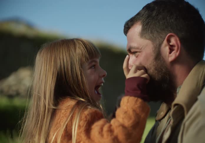 Father with beard and brown jacket plays with daughter in the countryside