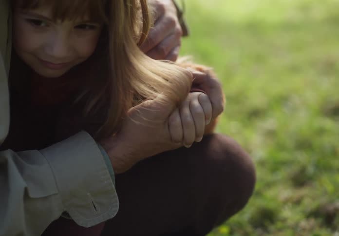 A young girl sits in her dads lap outside and they hold hands