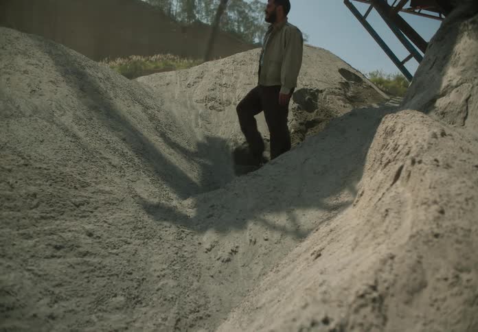 A man walks down a pile of dirt under a conveyor belt
