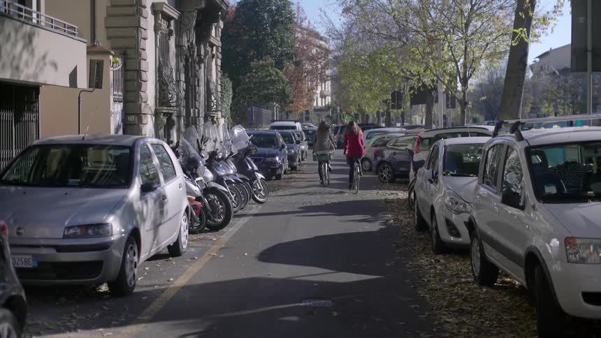 Two women riding bicycles down a city street in the fall