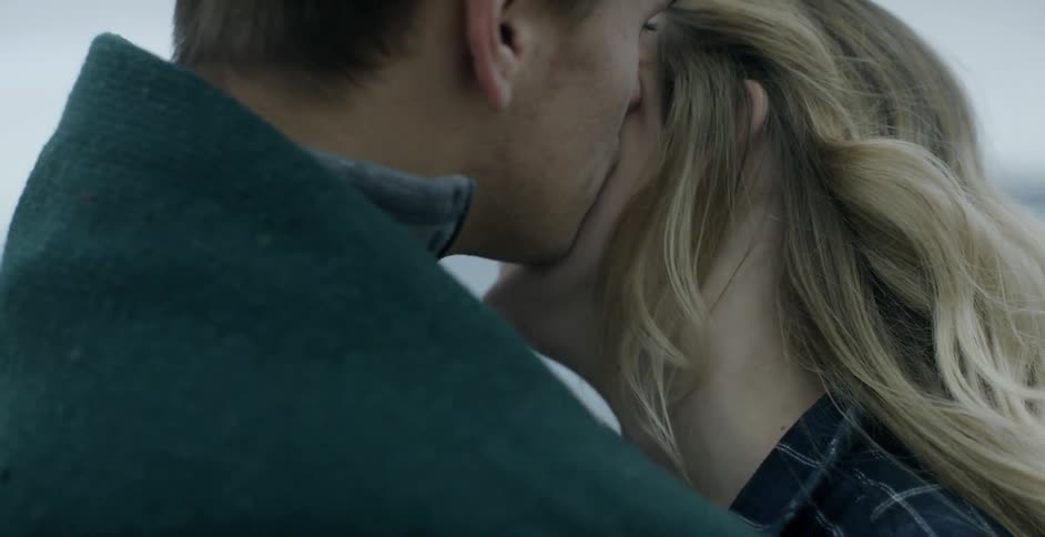 A woman is smiling and laughing as she is hugged and kissed by a man
