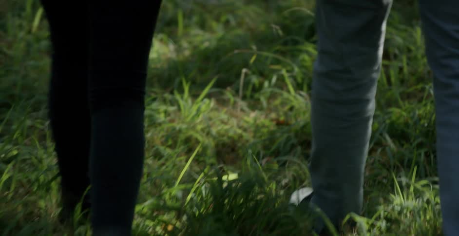 Two people walk along a grass field