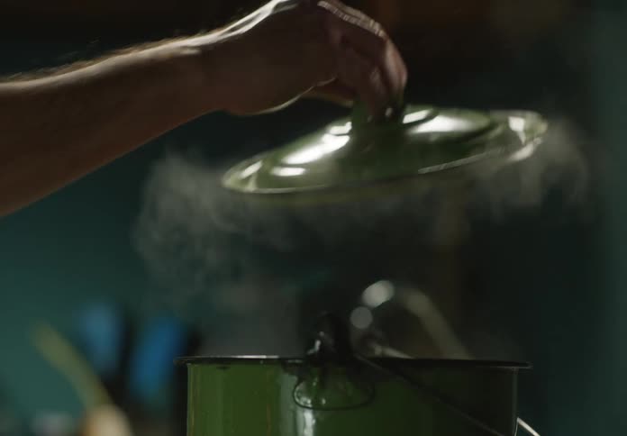 A man removes the lid from a dutch oven while cooking at home