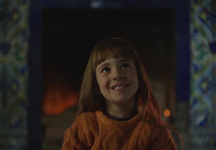A little girls laughs as she sits in front of a fireplace