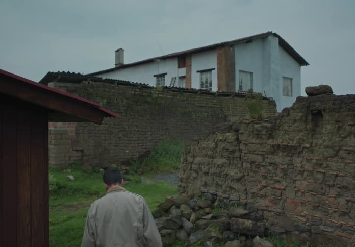 A man walks on a lawn in front of a rural home