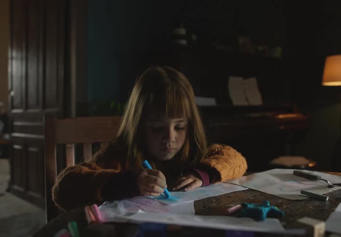 Girl sitting at the table in the living room of a house drawing with colored chalk
