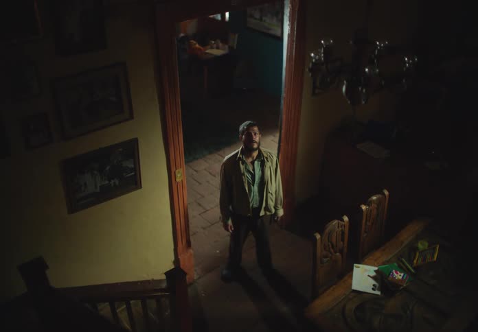 A man stands in a home and looks up the stairs and then heads to the stairwell