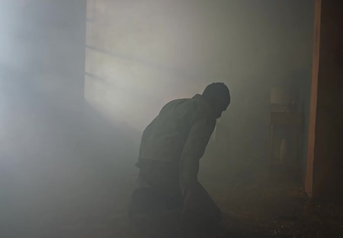 A man walking in a smoky room falls to his knees
