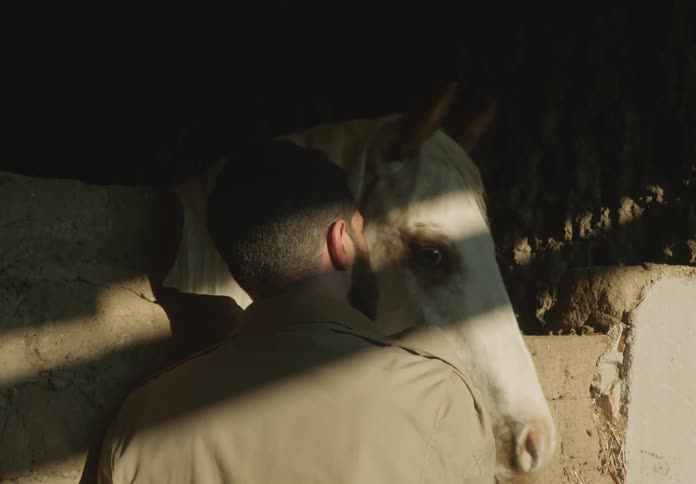 A man petting a white horse near a dirt wall