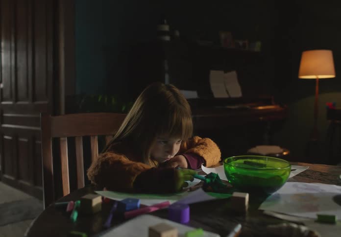 A little girl looks bored as she sits at a table and colors