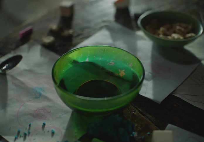 Warm liquidin one of two bowls on table sprinkled with pigment sloshes as surface vibrates