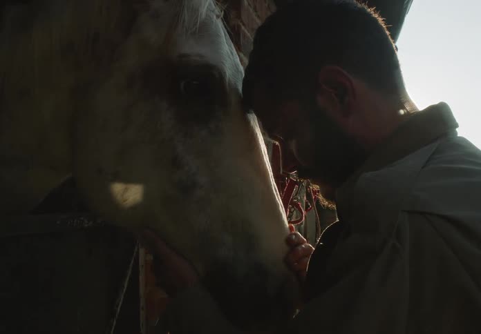 Man pets horse hanging its head out of its stall with semi in the background
