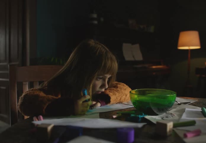 A young kid is sitting by the table and is drawing on a piece of paper