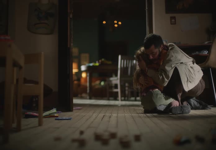 A father is playing around with his young daughter as they hug and then crawl on the floor to the other room