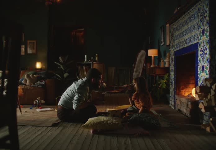 Father and child sit on the floor in front of the fireplace playing with toys as father playfully pokes daughters nose