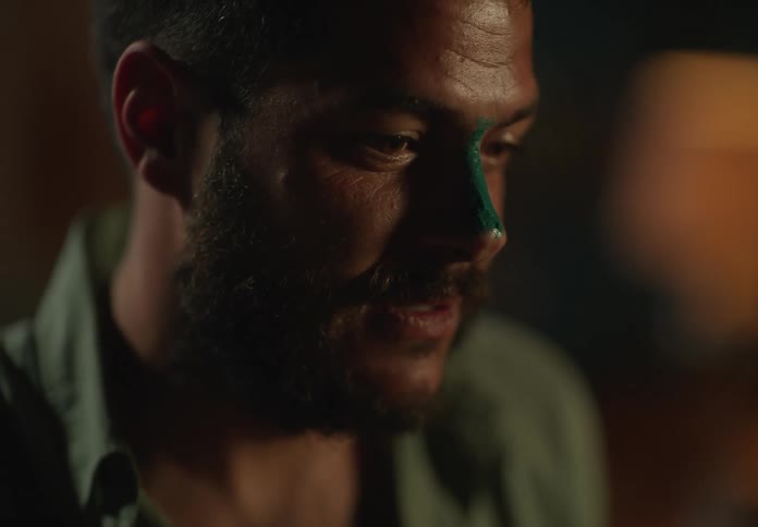 A man with green paint on his nose turns his head and laughs and talks
