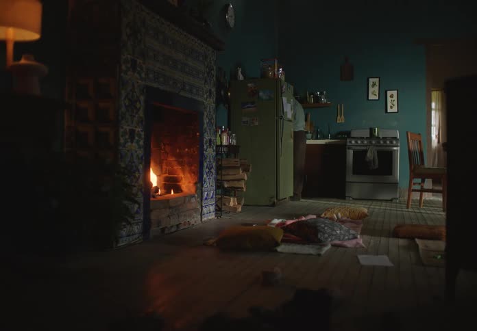 A man is shown looking around his kitchen as a fireplace blazes in the background