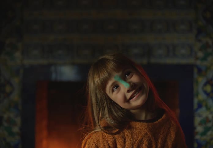 A little girl with makeup on her nose is making silly faces as she sits in front of a fireplace