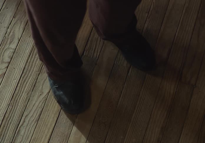 Person wearing black shoes and brown pants standing on hardwood flooring