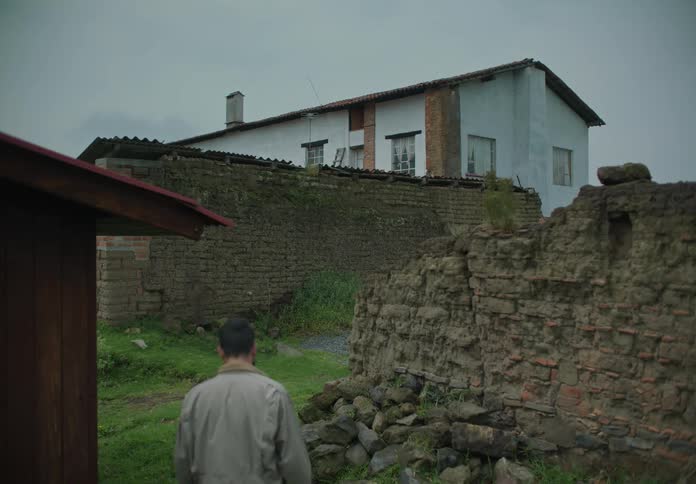 A man in a jacket walks around a damaged wall towards a residential building